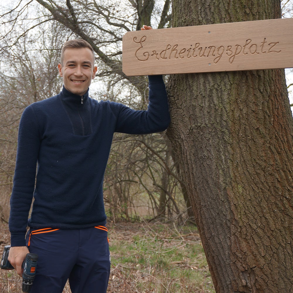 Mitarbeiter Jan neben einem neuen angebrachten Schild auf einem Erdheilungsplatz